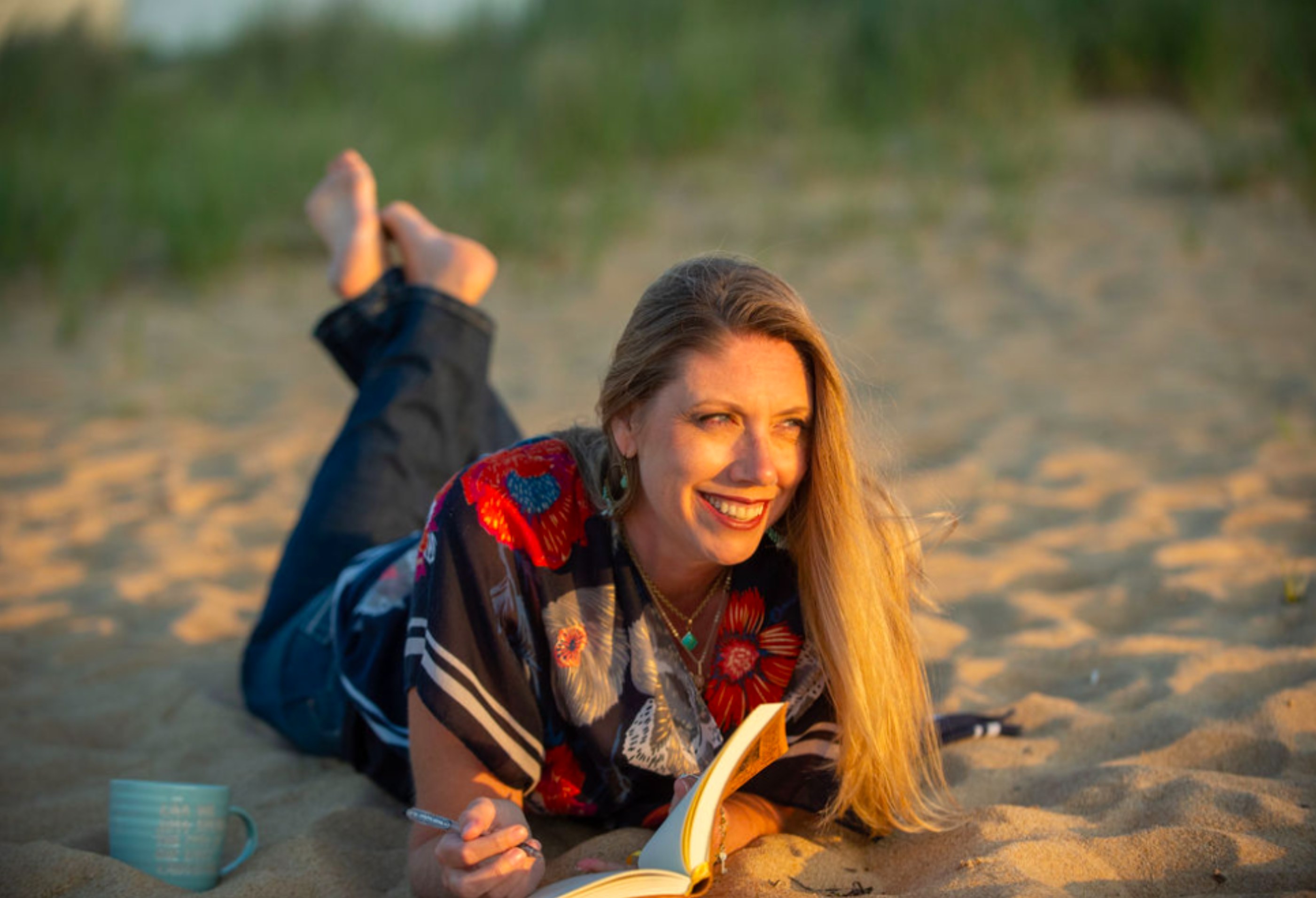 Rachelle Taylor lying on the beach at sunset, writing in a notebook